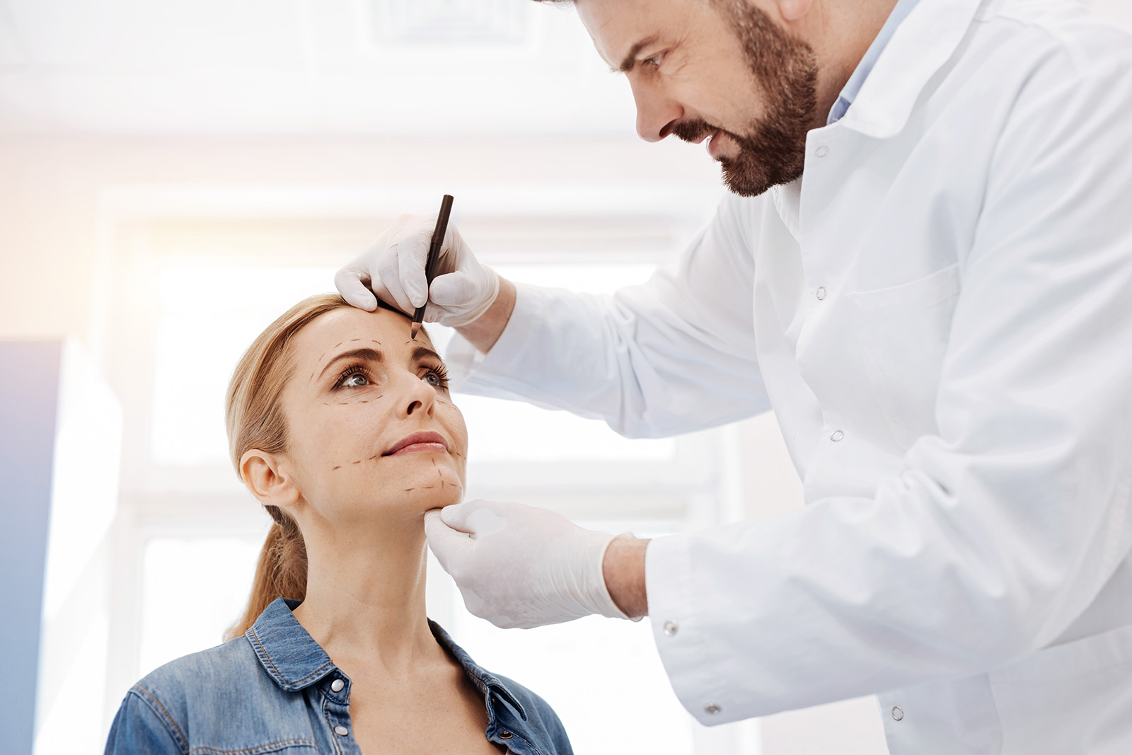 Serious plastic surgeon drawing marks on his patients face